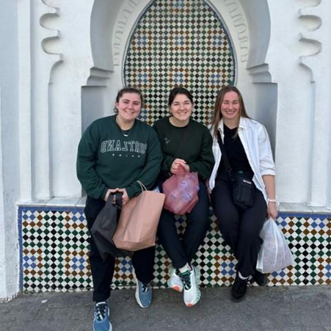 三名女学生在摩洛哥建筑前摆姿势. 照片设置在蓝色背景下.